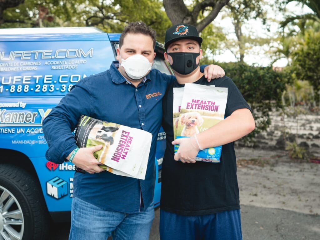Petland Texas picture of Petland owner, Luis Marquez and a pet owner holding bags of dog food and standing in front of a blue van.