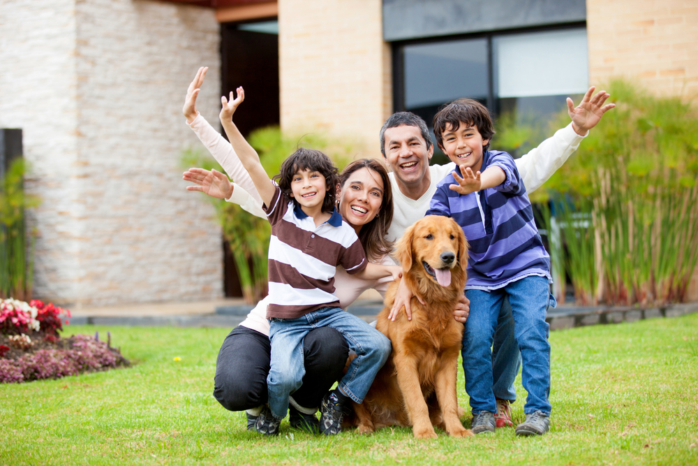 A happy family poses for the camera outside with their super golden Golden Retriever family dog in front of them. 