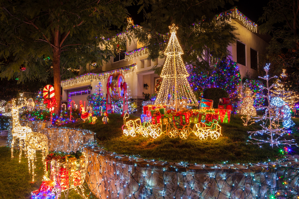 A residential house decorated with Christmas lights and holiday displays brightens the street at night.